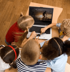 Children gathered around a laptop watching a video of two people biking;