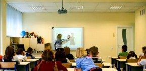 Teacher teaching class of students using interactive whiteboard;